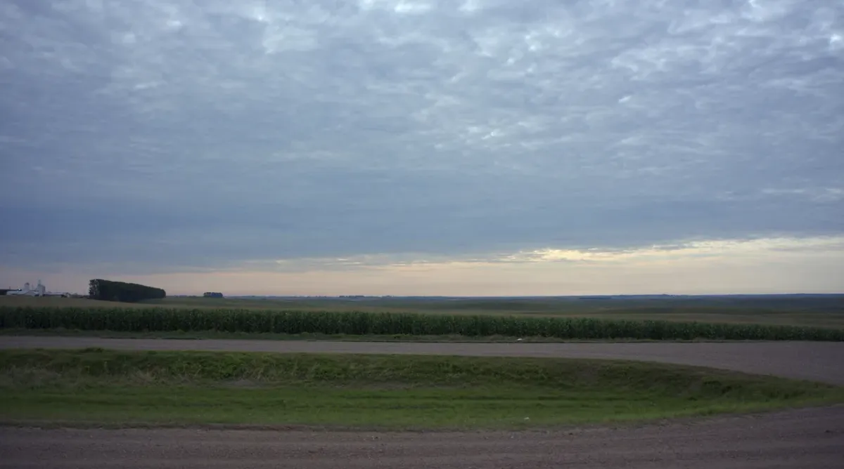 Rolling Iowa farmland and a gravel section-line road under a layered cloud sky near Des Moines, Iowa