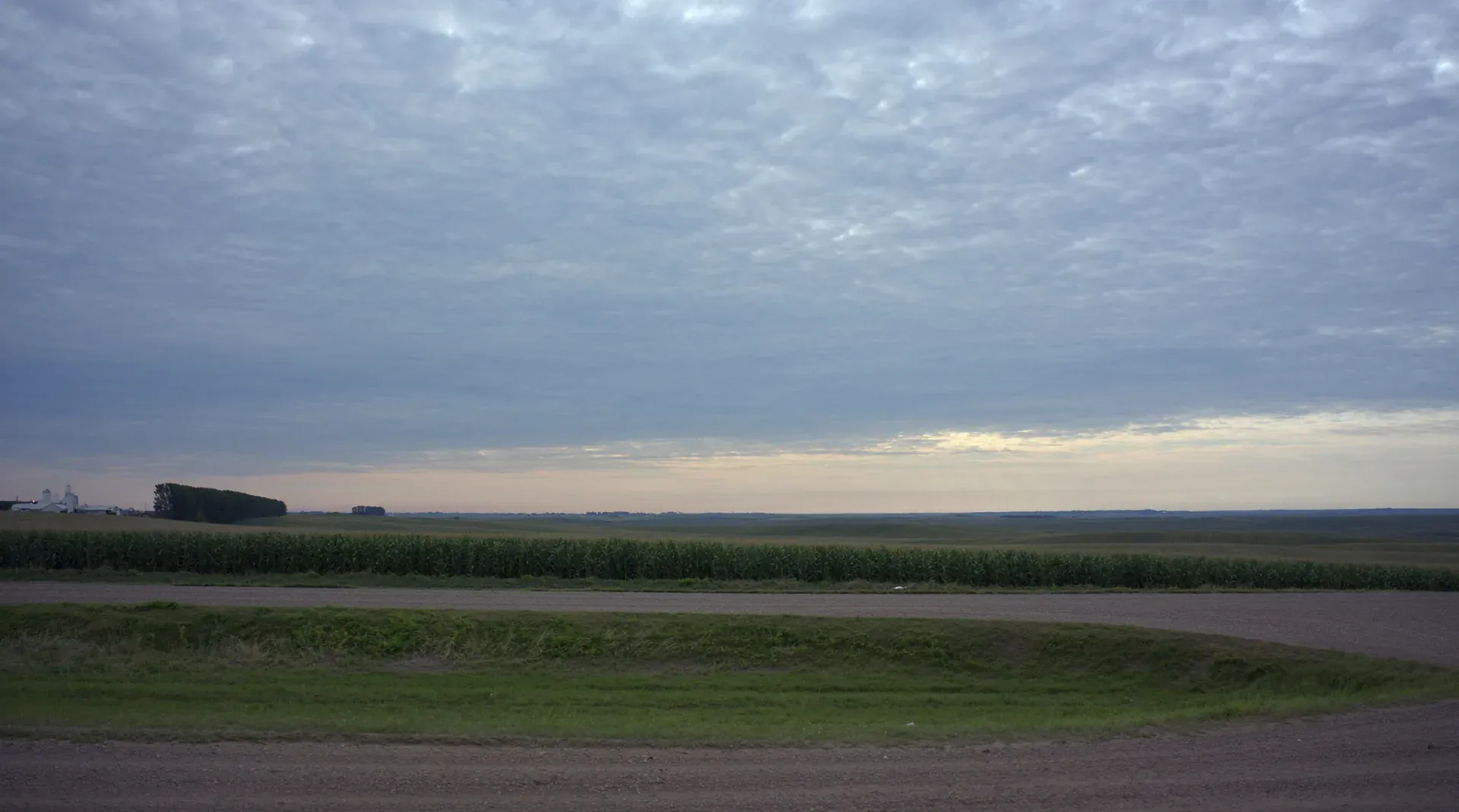 Rolling Iowa farmland and a gravel section-line road under a layered cloud sky near Des Moines, Iowa